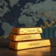 Gold bars on dark surface with world map and oil chart in background