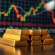 Gold bullion bars with a financial chart display in the background, representing gold's response to Federal Reserve policy.