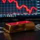 Gold bar and US dollar bills with a red price chart in the background, representing a market decline.