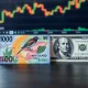 New Zealand Dollar and US Dollar banknotes on a desk with a financial chart in the background.