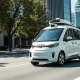 White robotaxi with roof sensors driving on a sunny city street