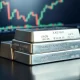 Silver bullion bars on a reflective surface with a financial chart in the background.
