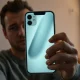 Person holding iPhone with AI assistant interface glowing on screen, thoughtful expression.