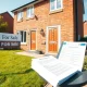A brick semi-detached house with a For Sale sign and property documents on the porch, representing the UK home-selling process.