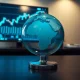 Glass globe of the world on a desk with a financial chart on a computer monitor in the background.