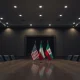 Empty diplomatic meeting room with US and Iranian flags on opposite sides of a table.