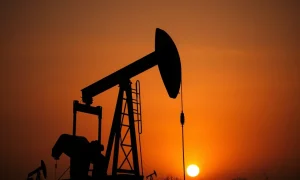 Oil pumpjack silhouetted against a hazy sunset sky, representing volatile crude oil markets.