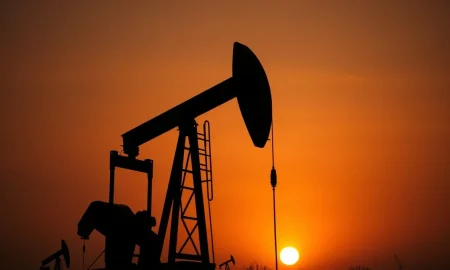 Oil pumpjack silhouetted against a hazy sunset sky, representing volatile crude oil markets.