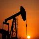 Oil pumpjack silhouetted against a hazy sunset sky, representing volatile crude oil markets.