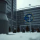 European Central Bank headquarters in Frankfurt on a cloudy day, with a blurred industrial silhouette in the foreground representing energy pressure.