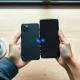 Person holding iPhone and Google Pixel 10 with wireless data transfer animation between them on a desk