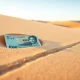 Japanese yen banknote partially buried in sand with a faint line drawn in the sand nearby