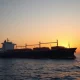 Oil tanker in the Strait of Hormuz at sunset with Iranian coastline in background