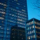 Two office buildings at twilight, one large and brightly lit, another smaller and dimly lit, representing private equity market concentration.