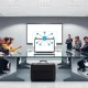 Corporate meeting room with startup and enterprise teams facing off over a laptop showing a network diagram