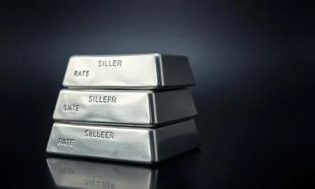 Stack of polished silver bullion bars on a dark reflective surface with soft lighting.
