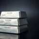 Stack of polished silver bullion bars on a dark reflective surface with soft lighting.
