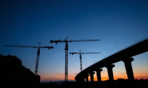 Construction cranes at an infrastructure project site at dusk, representing AECOM's project portfolio.