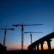 Construction cranes at an infrastructure project site at dusk, representing AECOM's project portfolio.
