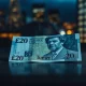 British Pound Sterling banknote on a dark surface with a blurred London financial district background.