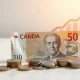 Canadian dollar banknotes and coins with a subtle upward chart in the background