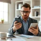George Kamel looks at a smartphone at his desk, illustrating his analysis of Trump Accounts.