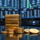 Gold bars and coins on a reflective surface with a blurred financial trading floor in the background