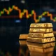 Gold bars stacked with a blurred financial market chart in the background