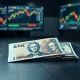 Japanese yen banknotes and US dollars on a trading desk with charts in background