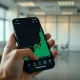 Smartphone displaying a cryptocurrency trading chart with a sharp green upward price spike for Momentum (MMT) token.
