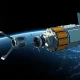 A robotic satellite servicing vehicle with robotic arms approaches a large communications satellite in Earth orbit.
