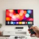 Person using a remote control in front of a TV screen showing a streaming interface