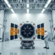 Engineers in a cleanroom working on a large satellite at a European aerospace facility.