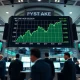 Stock market traders watching an electronic board with rising green numbers during a record-high trading session