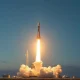 SpaceX Falcon 9 rocket launching at dawn with Starlink satellites visible in the sky