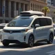 A Waymo Ojai robotaxi driving on a city street, equipped with cameras and sensors.