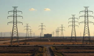 High-voltage transmission towers and power lines in front of a data center, illustrating AI infrastructure demands.