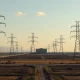 High-voltage transmission towers and power lines in front of a data center, illustrating AI infrastructure demands.