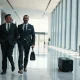 Two officials in suits walking through a corporate headquarters lobby after US-China trade talks