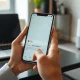 Hands holding a smartphone showing an AI assistant interface in a bright modern home setting.