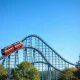 ArieForce One steel roller coaster with red and yellow trains against a blue sky at an amusement park.