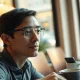 Person wearing slim display-free smart glasses with a small indicator light on the temple arm